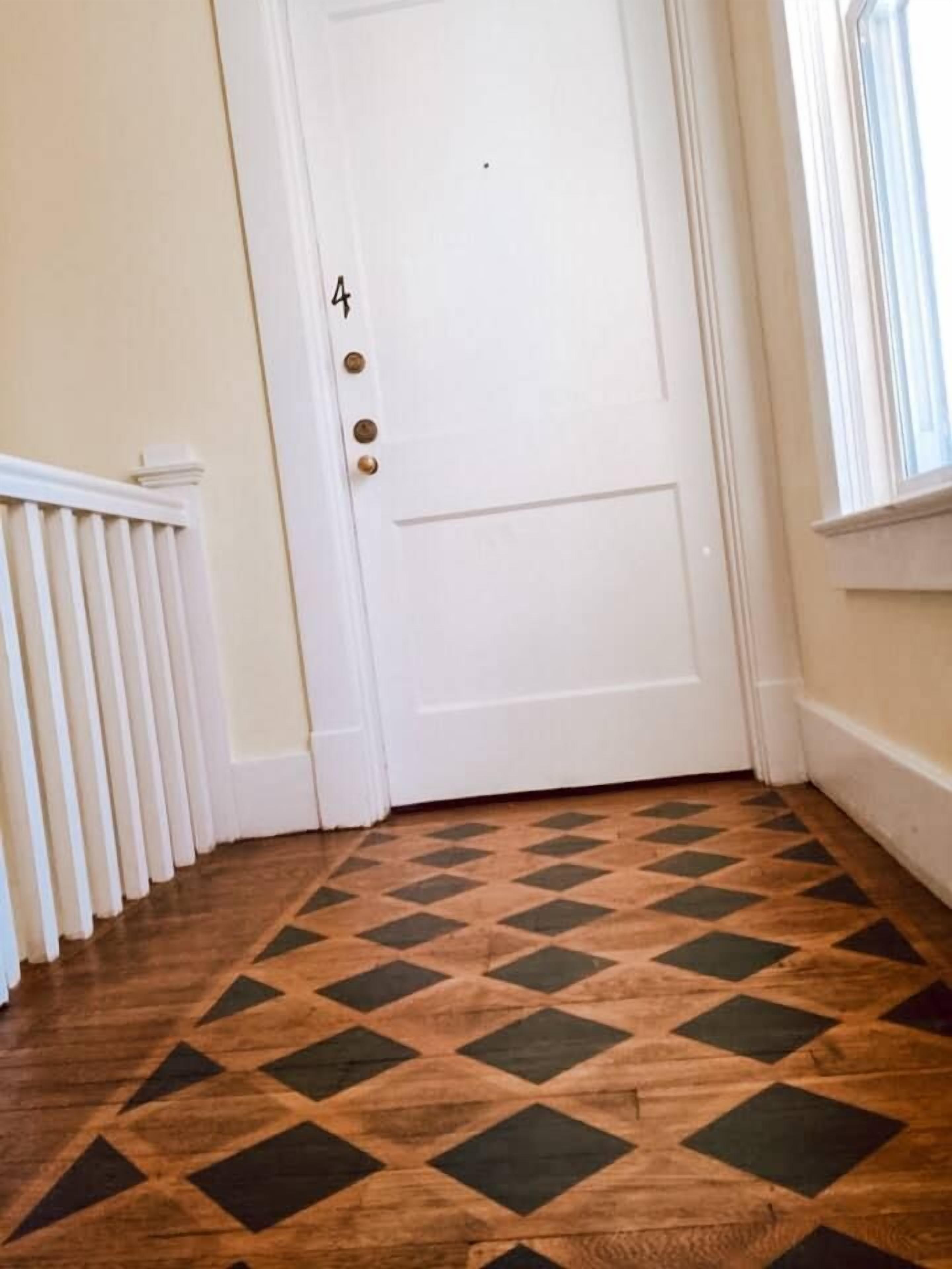 Un couloir avec une porte blanche portant le numéro 4, un radiateur et un sol à motifs.