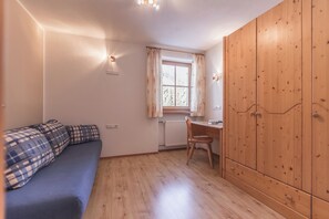 Ein Zimmer mit einer Couch, einem Holzschrank, einem Schreibtisch und einem Fenster mit Vorhängen.