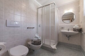 Ein Badezimmer mit Toilette, Bidet, einer Duschkabine und einem Waschbecken mit Spiegel.