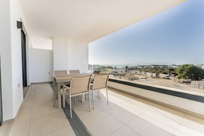 A balcony with a table and chairs, a view of the city, and a clear sky. - Green Fairway by IIM (AN)