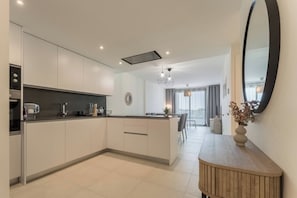 A modern kitchen with a central island, a dining area with a view, and a large mirror. - Green Fairway by IIM (AN)