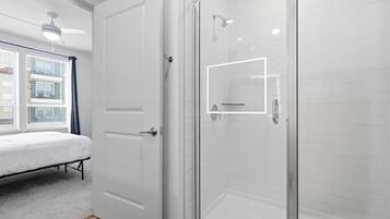A modern bathroom with a glass shower enclosure, a white toilet, and a bed with a white mattress.