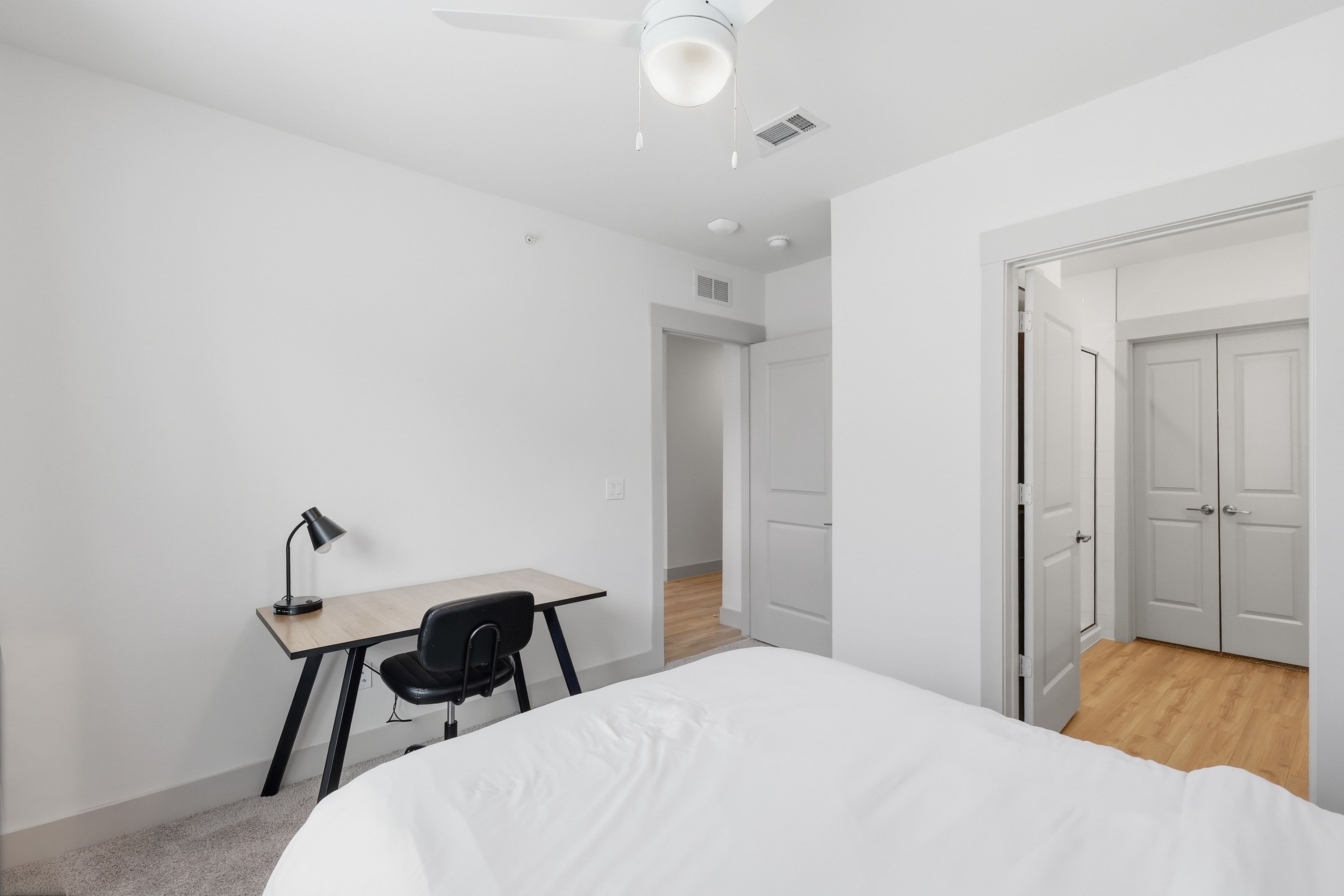 A bedroom with a bed, a desk, and a chair. There is a door leading to another room.
