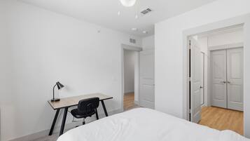 A bedroom with a bed, a desk, and a chair. There is a door leading to another room.