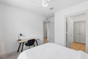 A bedroom with a bed, a desk, and a chair. There is a door leading to another room. - Modern 2BR near PGA & Universal Studios (Frisco)