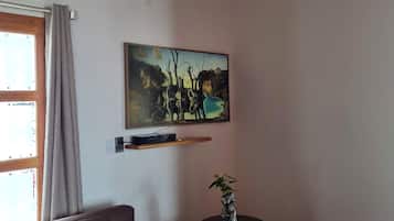 A living room with a sofa, a small table with a plant, a painting on the wall, and a window with curtains.