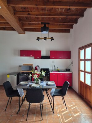 A kitchen with red cabinets, a dining table set for four, and a ceiling with exposed wooden beams.
