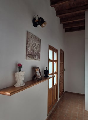 A hallway with a wooden bench, a framed picture, a vase with a flower, and a wall-mounted light fixture.