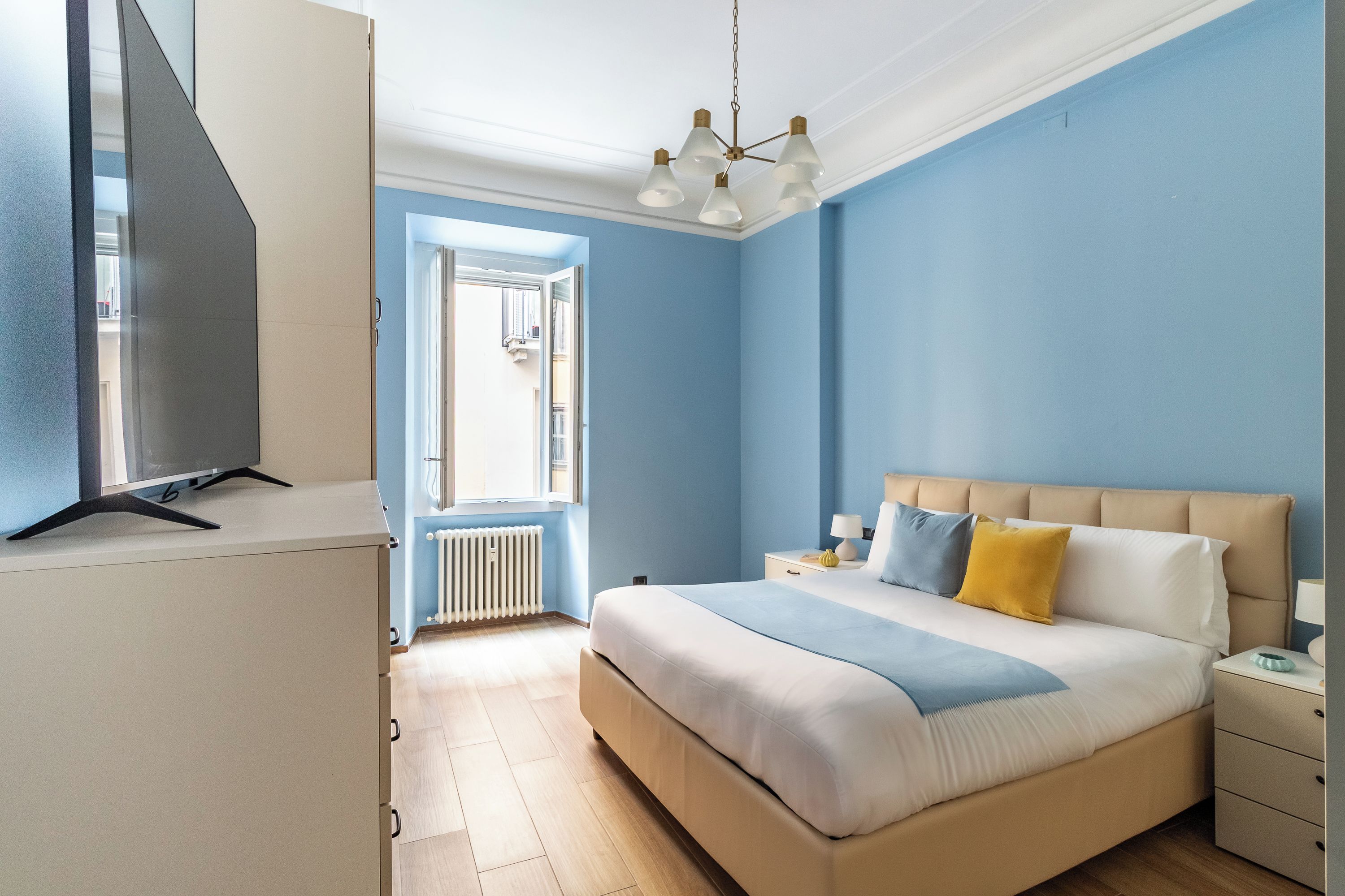 A bedroom with a bed, bedside tables, a radiator, and a window.