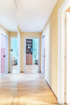 A spacious hallway with a wooden floor leading to a room with a bookshelf and a sofa. - Corso Buenos Aires 61 (Milan)