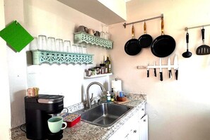A kitchen with a coffee maker, sink, and hanging pots. - Mission Beach Ocean View 1 bdrm w/ Large Patio 716 (San Diego)