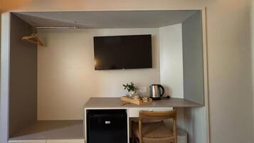 Una habitación compacta con kitchenette, un televisor de pantalla plana en la pared y un pequeño rincón de descanso con una silla y una mesa.