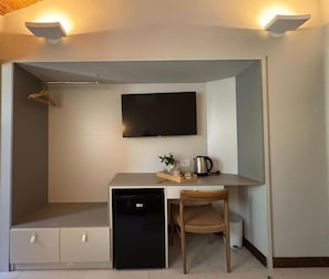 A compact room with a kitchenette, a flat-screen TV mounted on the wall, and a small seating area with a chair and a table.