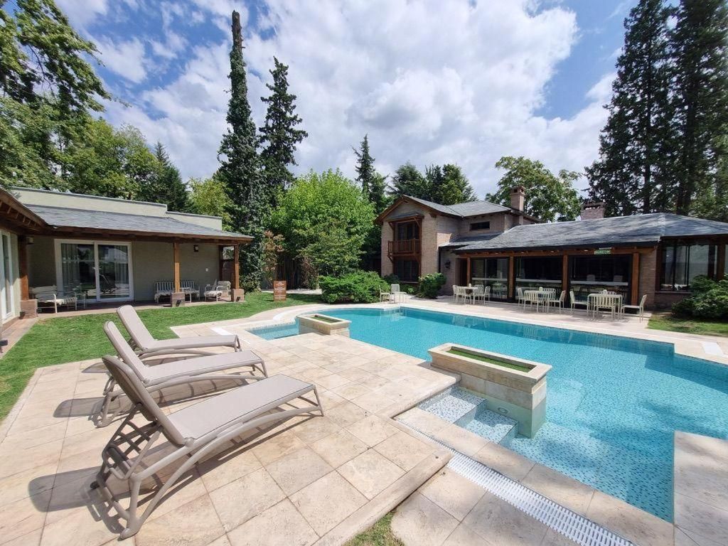 Una piscina con sillones de descanso y un patio, rodeado de árboles y edificios.