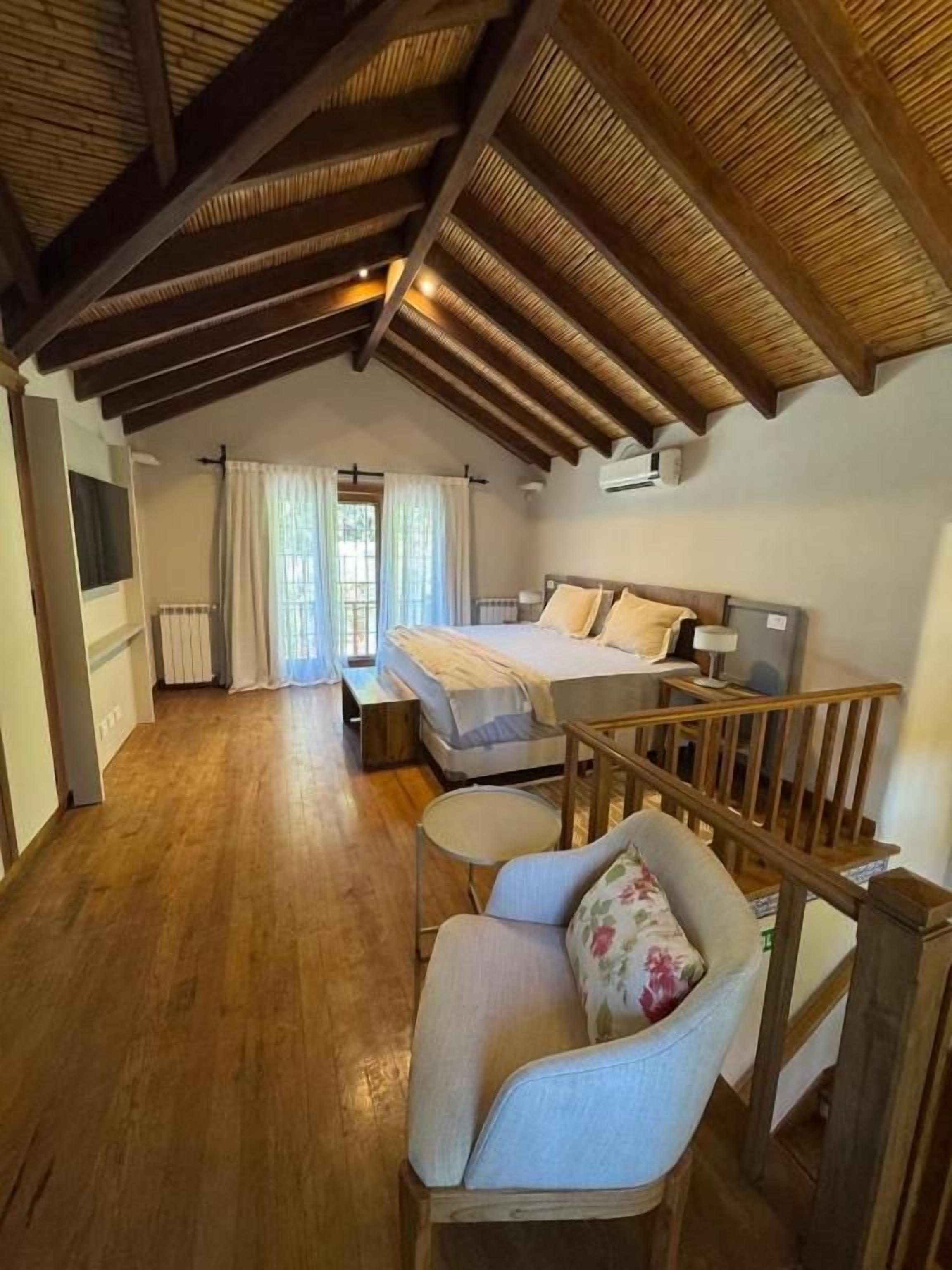 Un dormitorio con techo de madera, una cama, una silla y un ventanal con cortinas.