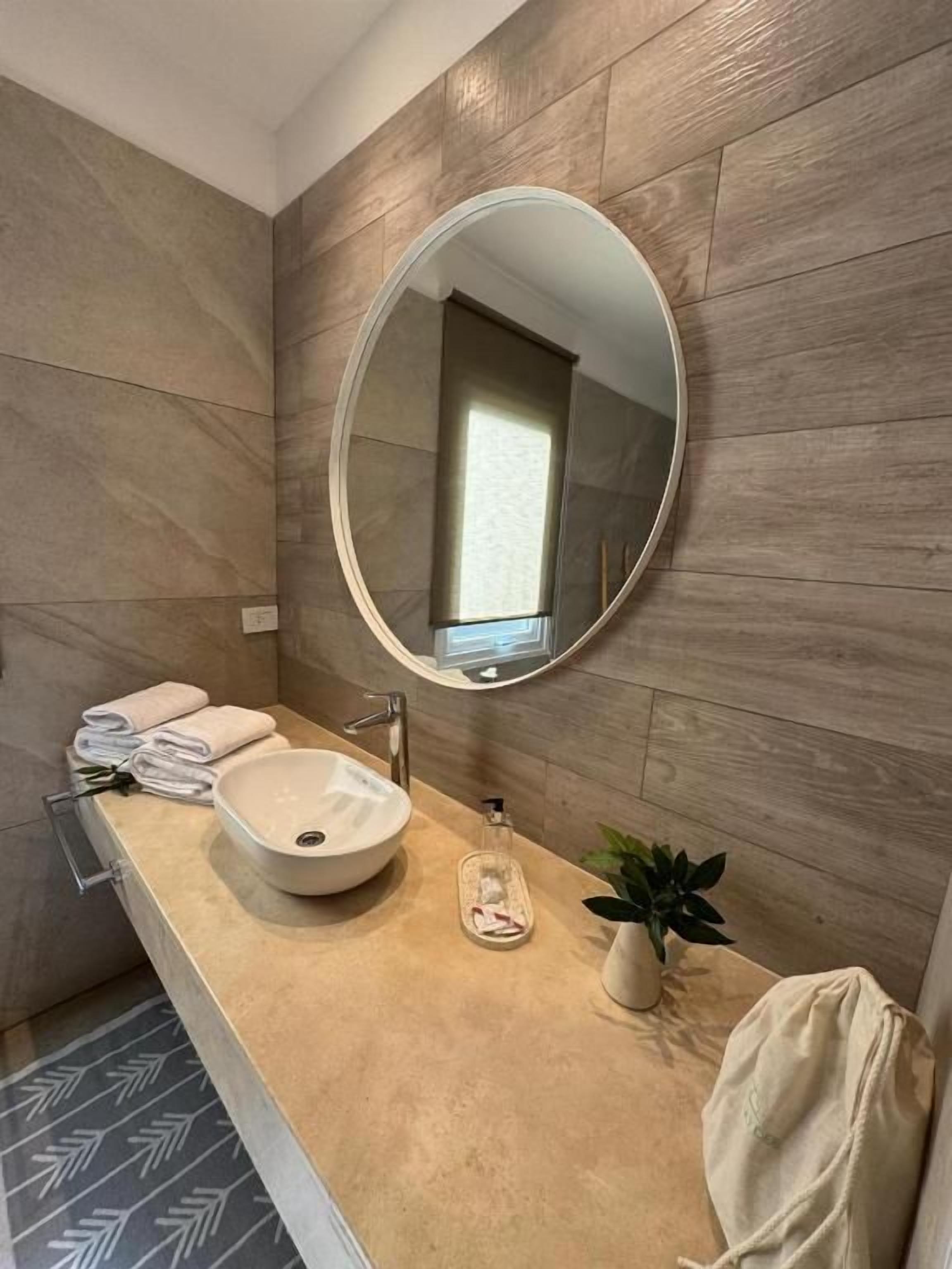 Un baño con un espejo redondo, un lavamanos y un perchero para toallas.