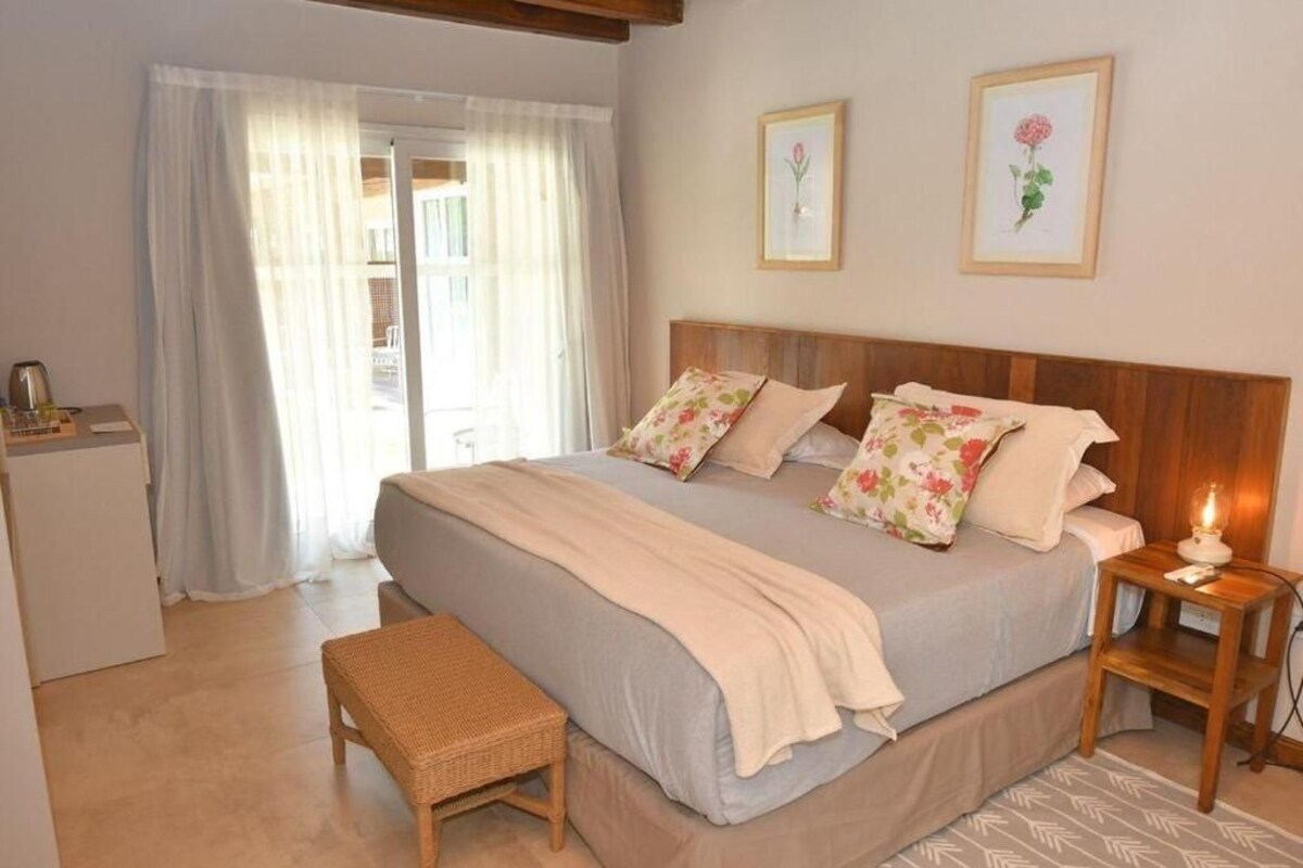 A bedroom with a bed, bedside table, bench, and a view of the outside.