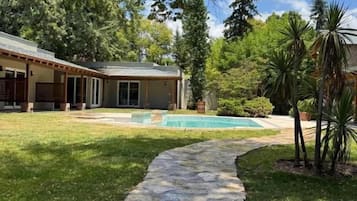 Un sendero de piedra que lleva a una casa con piscina, rodeada de vegetación y árboles.