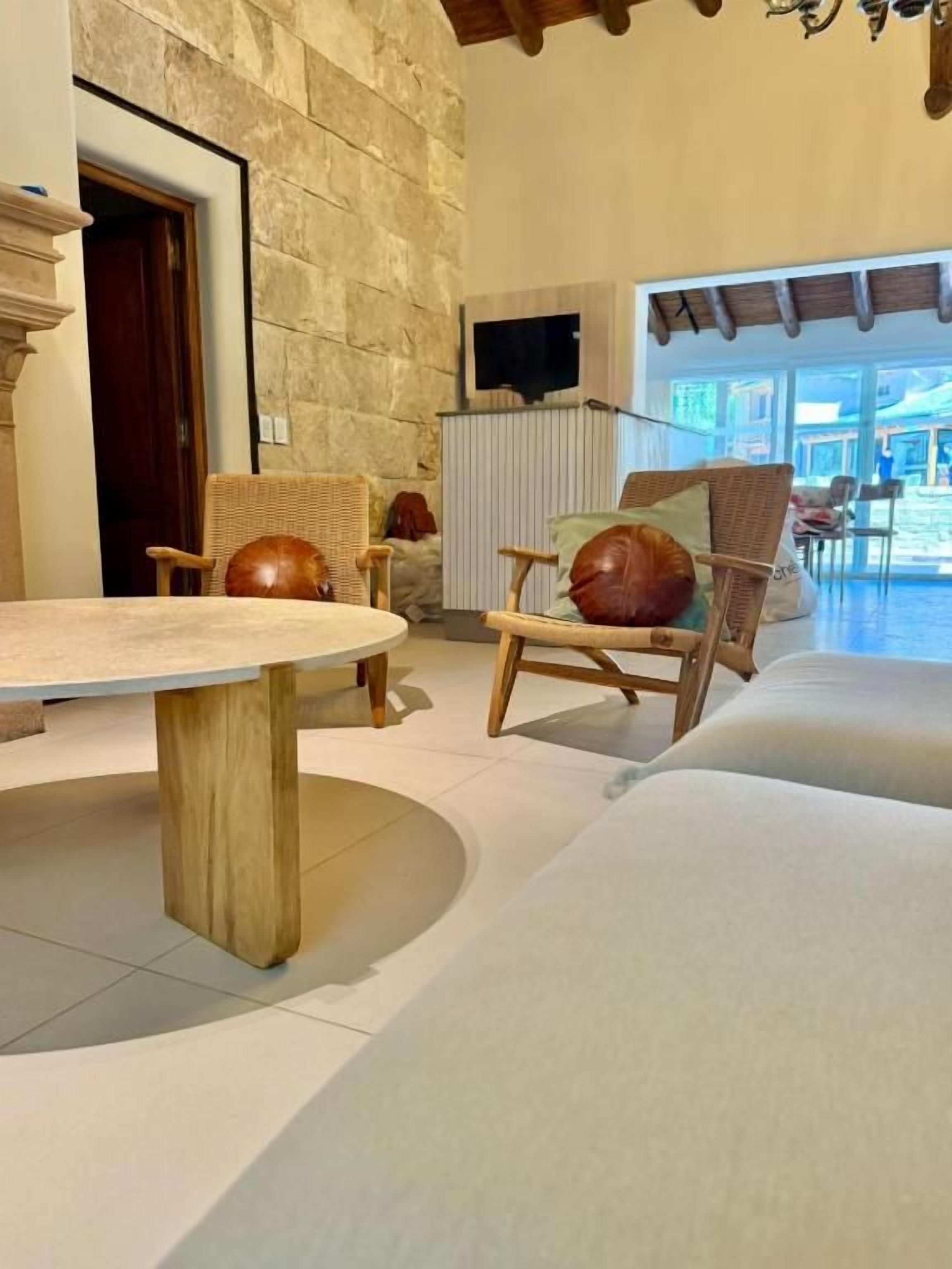 A room with a round table, wicker chairs, a sofa, stone walls, and a view through large windows.