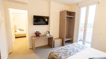 Habitación de hotel con cama, escritorio, televisión, armario y balcón.