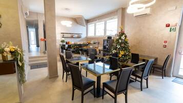 Un comedor con una mesa de vidrio rodeada de sillas, un árbol de Navidad y una cocina al fondo.