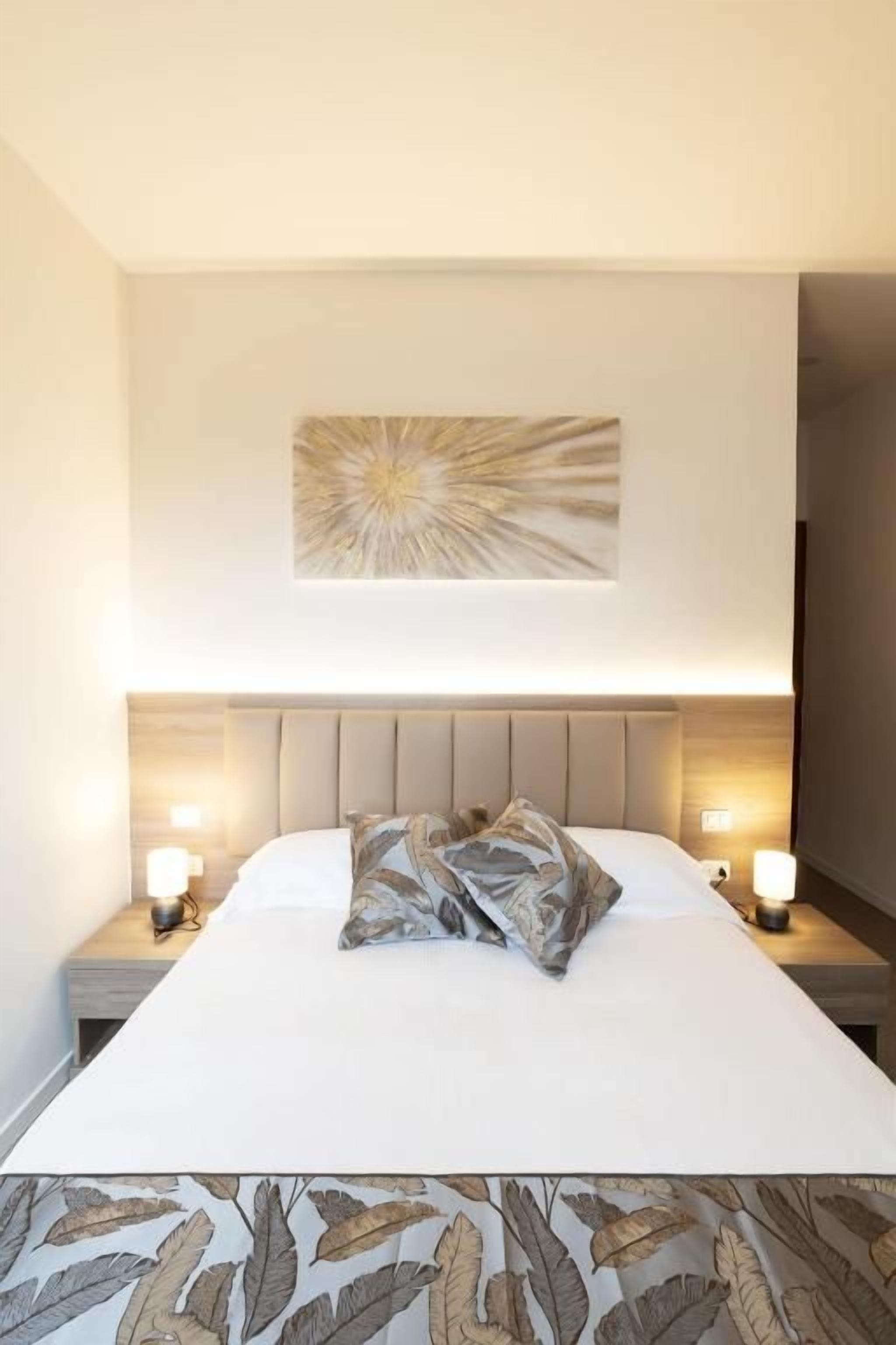 A hotel room with a large bed, a headboard, bedside lamps, and a wall-mounted artwork.