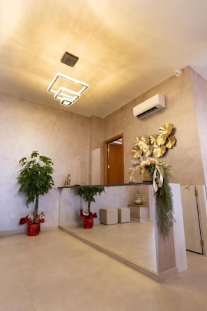 Zona de recepció amb disseny modern, inclou una taula d'informació, plantes en testos i una obra decorativa a la paret.