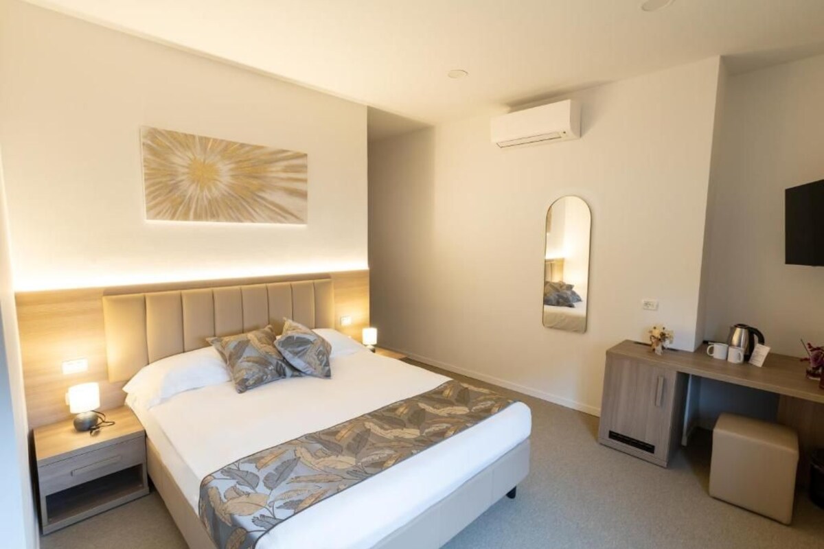 A hotel room with a bed, bedside table, lamp, mirror, and a small desk with a chair.