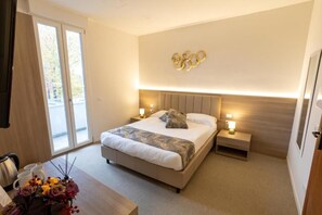 A modern hotel room with a large bed, bedside tables, a desk with a vase of flowers, and a wall-mounted Olympic rings decoration. - HOTEL RICHARD (Agliana)