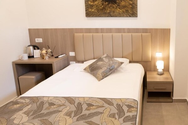 A hotel room with a bed, bedside tables, a nightstand, a lamp, and a wall-mounted artwork.