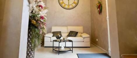 Un pasillo con un sofá blanco, un reloj de pared redondo y una planta decorativa.