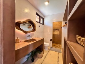 Un baño moderno con tocador de madera, un espejo grande y cabina de ducha de piedra.