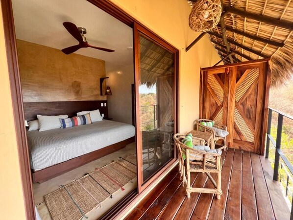 Una habitación con una cama, un ventilador de techo, una cesta tejida y una puerta de madera.