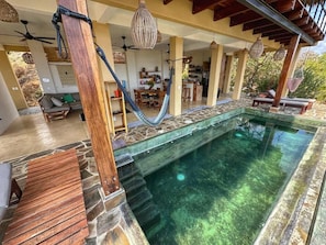 Zona de piscina con pared de piedra, terraza de madera y sillones de descanso.