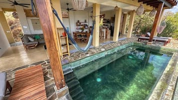 A pool area with a stone wall, wooden deck, and lounge chairs.