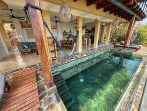 Zona de piscina con pared de piedra, terraza de madera y sillones de descanso.