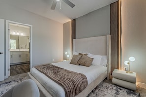 A modern hotel room with a large bed, bedside lamps, a ceiling fan, and a view into the bathroom. - Home Sweet Stay 2BD/2BA • Pool • Gym (Scottsdale)