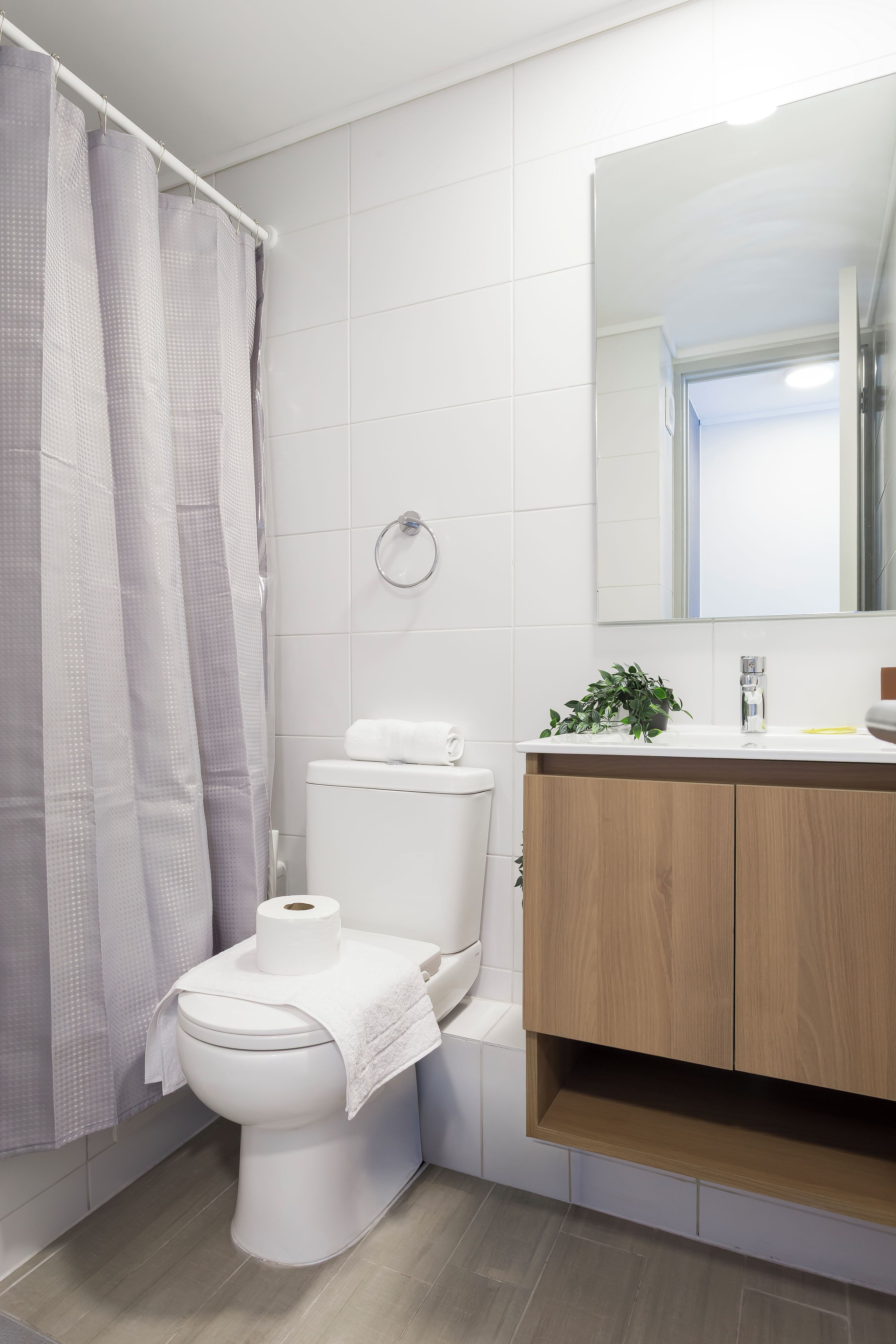 A bathroom with a toilet, a shower curtain, a towel, a toilet paper roll, a sink with a mirror, and a plant.