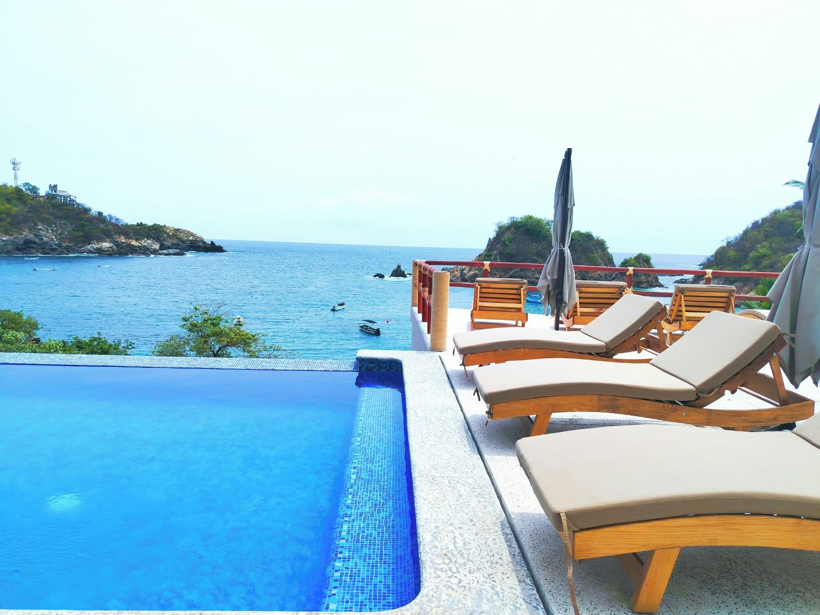 Un área junto a la piscina con sillones y sombrillas, con vista a un cuerpo de agua.