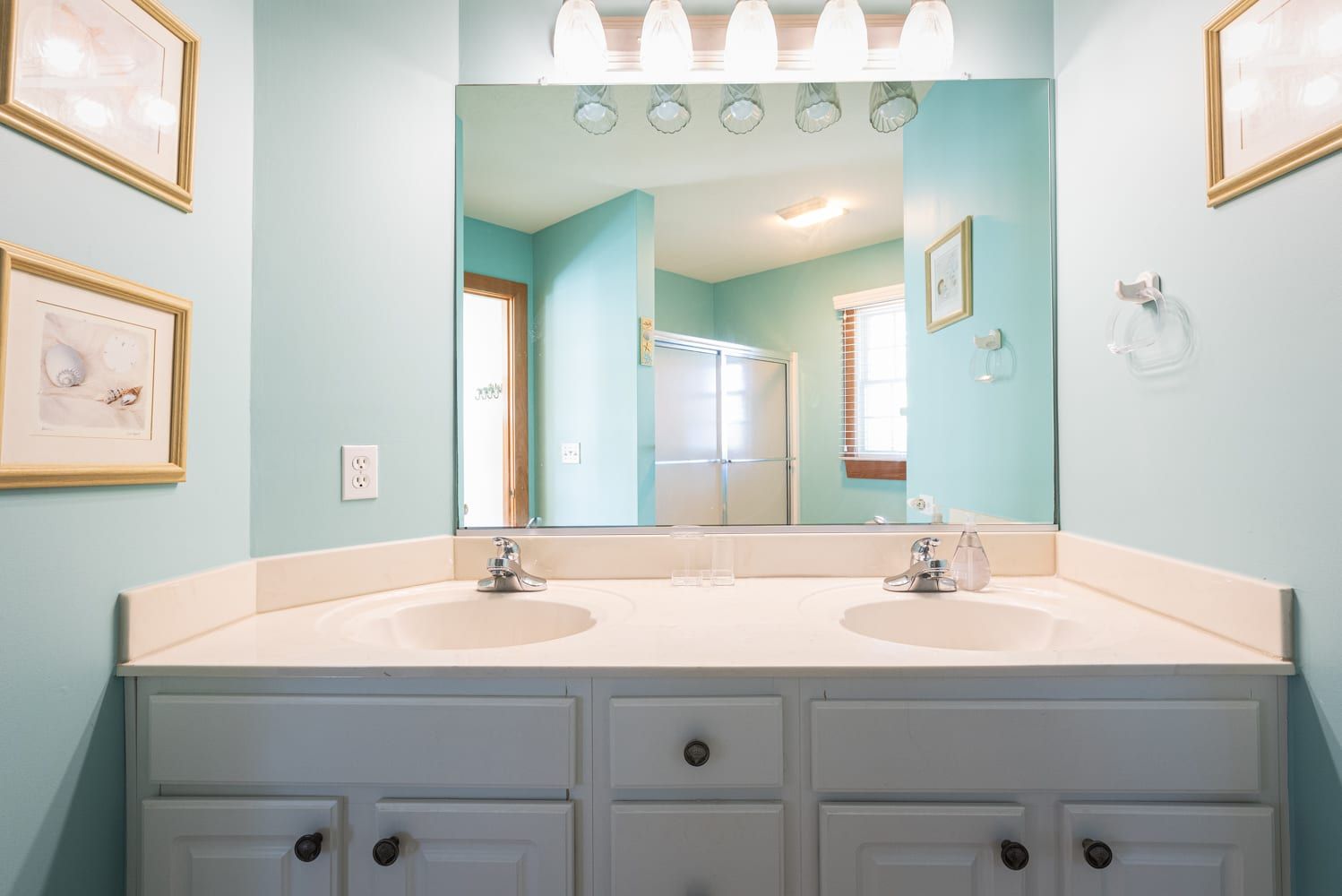 A bathroom with two sinks, a large mirror, and framed pictures on the wall.