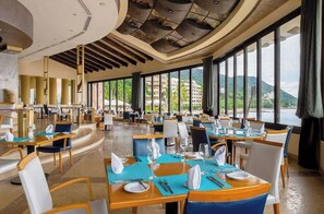 Un vaste espace dédié à la salle à manger, avec des tables dressées pour les convives, de grandes fenêtres offrant une vue sur l’extérieur et un design moderne au niveau du plafond.