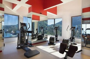 Une salle de sport moderne dotée de divers équipements d’exercice, de grandes fenêtres et offrant une vue sur la montagne.