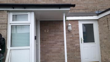 A residential entrance with a brick wall, a white door, and a window with shutters.