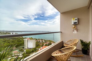 A balcony with wicker chairs, a water heater, and a view of a coastal cityscape.