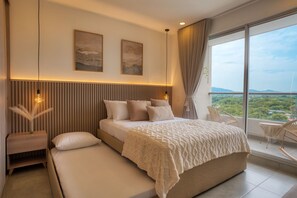 A modern bedroom with a large bed, a bedside table, a nightstand, and a view of a balcony with a cityscape.