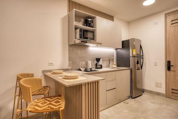 A modern kitchen with a built-in microwave, coffee maker, and refrigerator. There are two wicker chairs and a small bar area with a countertop.