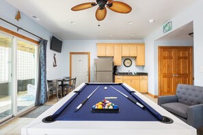 A pool table with pool balls, a ceiling fan, a kitchen area, and a seating area with a couch. - Walk to Beach w Pool, GameRm, Summer Availability! (Corolla)