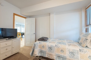 A bedroom with a bed, a television on a dresser, and a door leading to another room. - 2min Walk to Beach, Pool, Spa, Game Room, Big Yard (Corolla)