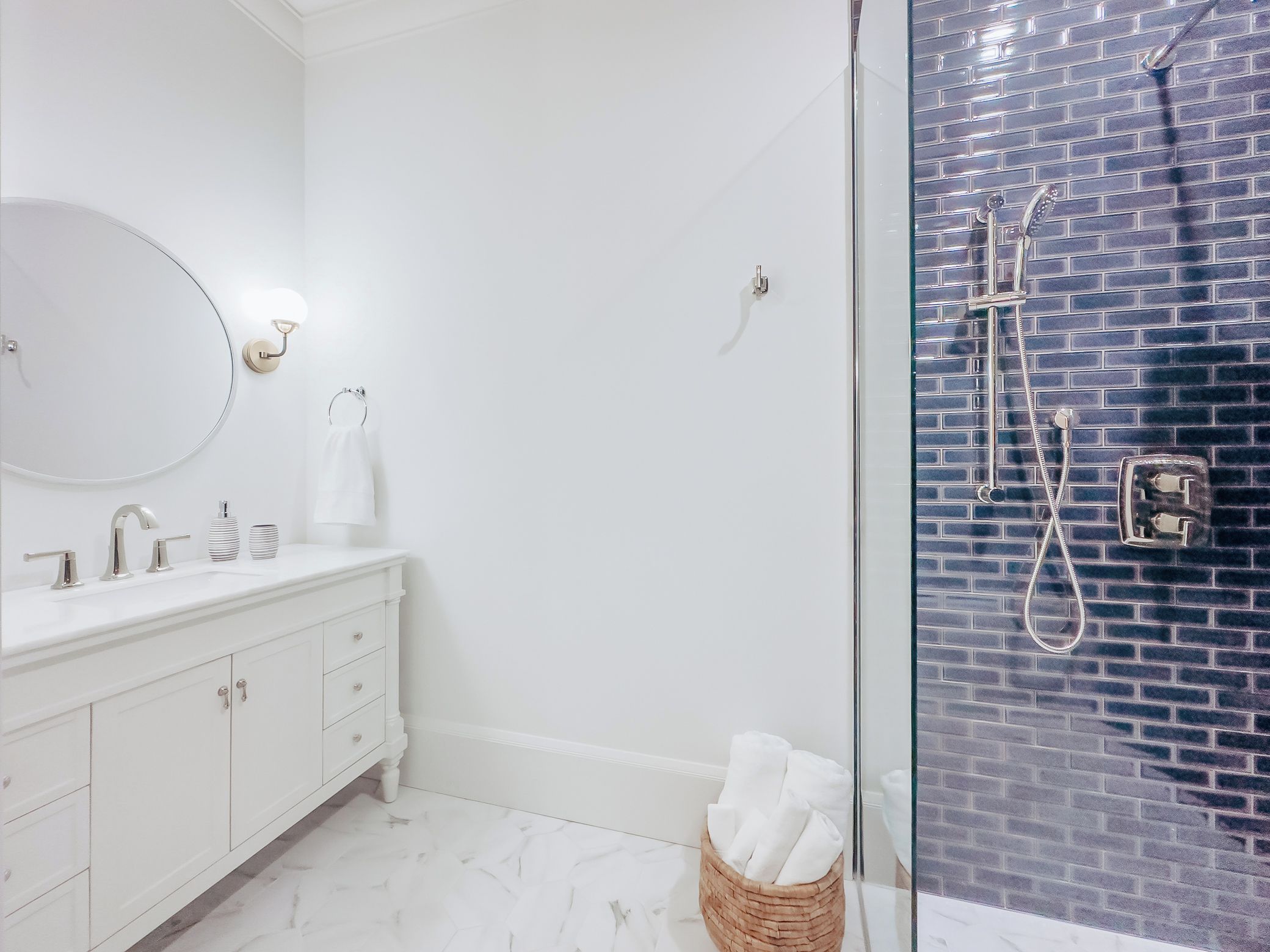 Une salle de bain moderne avec un meuble-lavabo blanc, un grand miroir et une douche en verre, le mur étant recouvert de carreaux bleus.