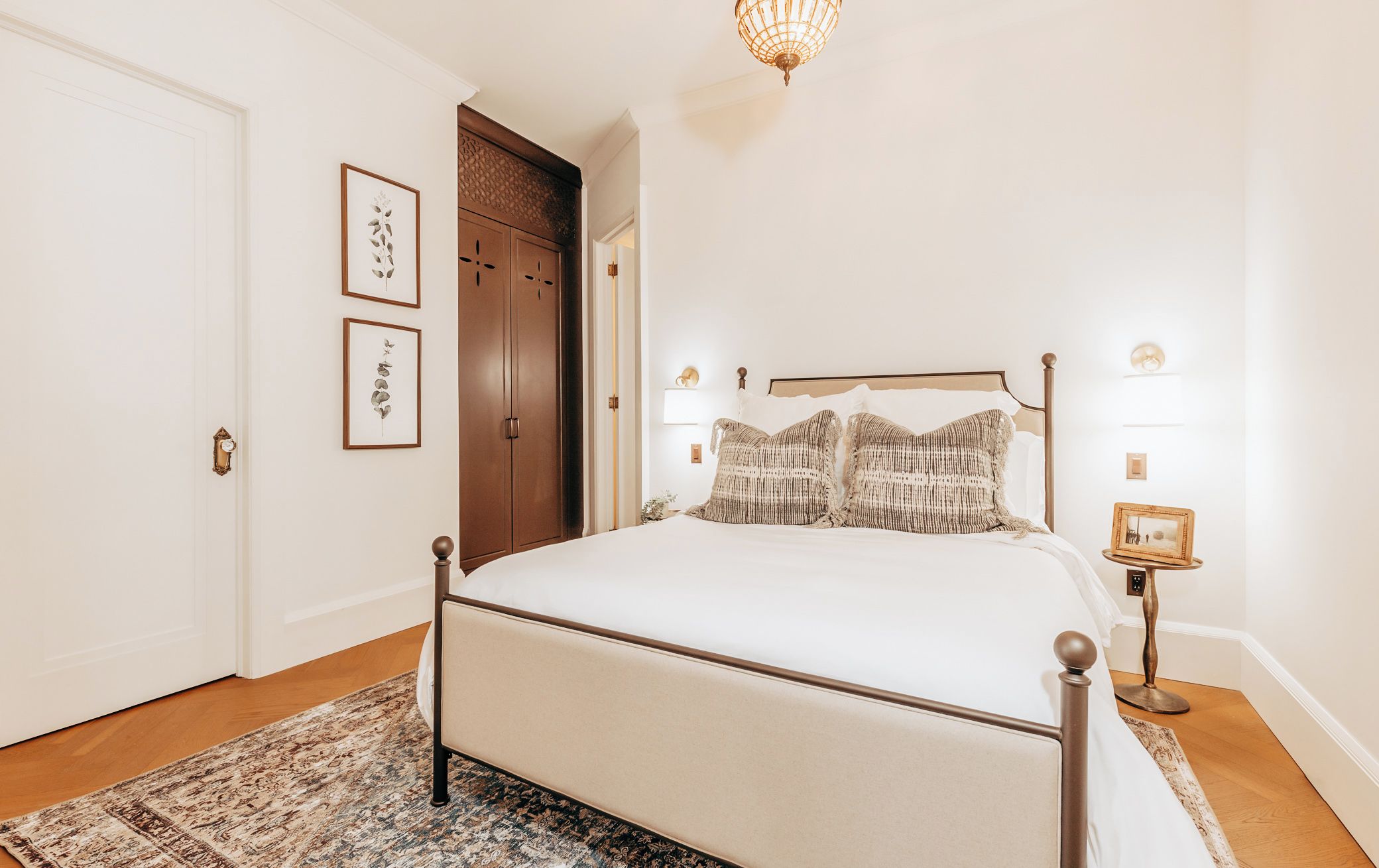 A bedroom with a bed, a nightstand, a lamp, and framed artwork on the wall.